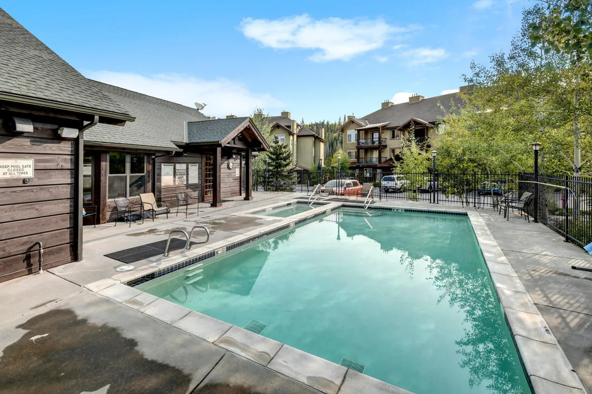A beautiful outdoor heated swimming pool surrounded by lounge chairs, with lush trees and modern building architecture in the background. The mood is relaxed and leisurely, inviting guests to swim or sunbathe while enjoying resort-style amenities.