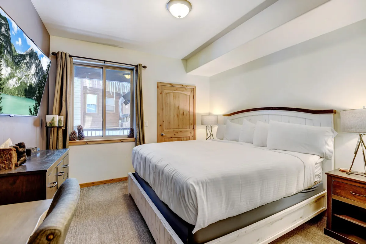 A spacious bedroom showcasing a large, inviting bed, a television for leisure, and a window offering mountain views. The setting is comfortable for both winding down and enjoying entertainment, with an emphasis on relaxation and privacy.