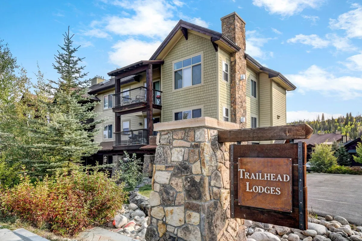 Here, the stone sign and wooden balconies are framed by lush greenery and the facade of the building, suggesting a welcoming entrance. The outdoor vibe hints at nearby nature, recreation, and neighborhood exploration.