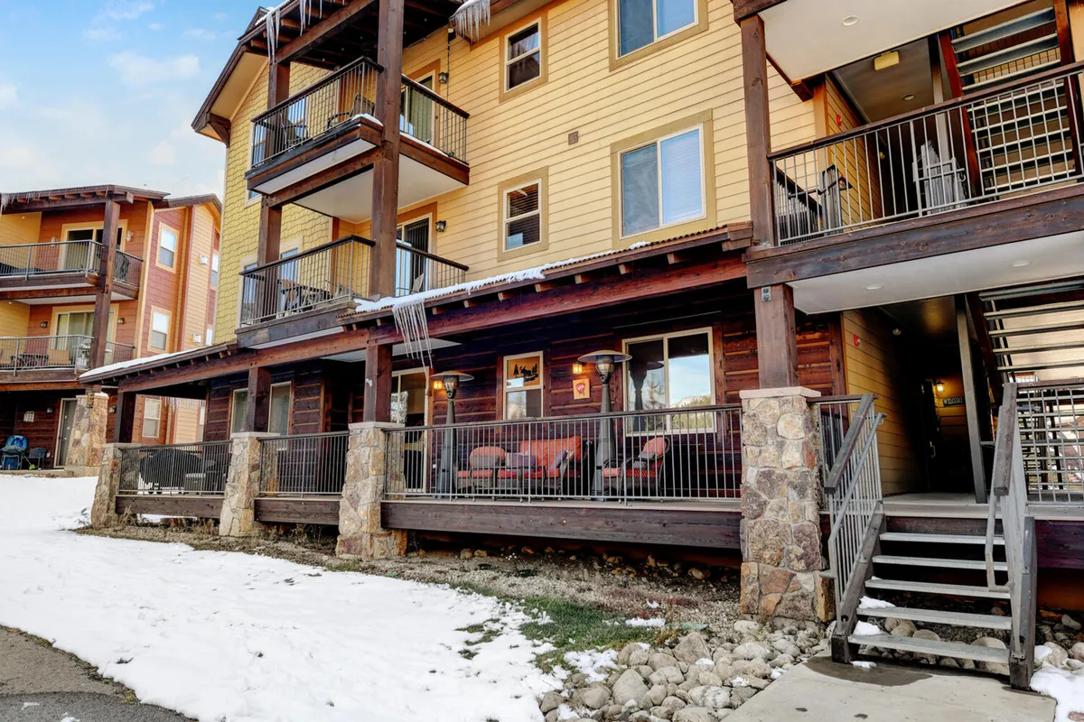 This image displays a welcoming wooden deck with stone pillars and balcony seating, all set against a backdrop of snow-covered ground. The exterior evokes a sense of gathering and relaxation, with outdoor spaces ideal for group activities in any season.