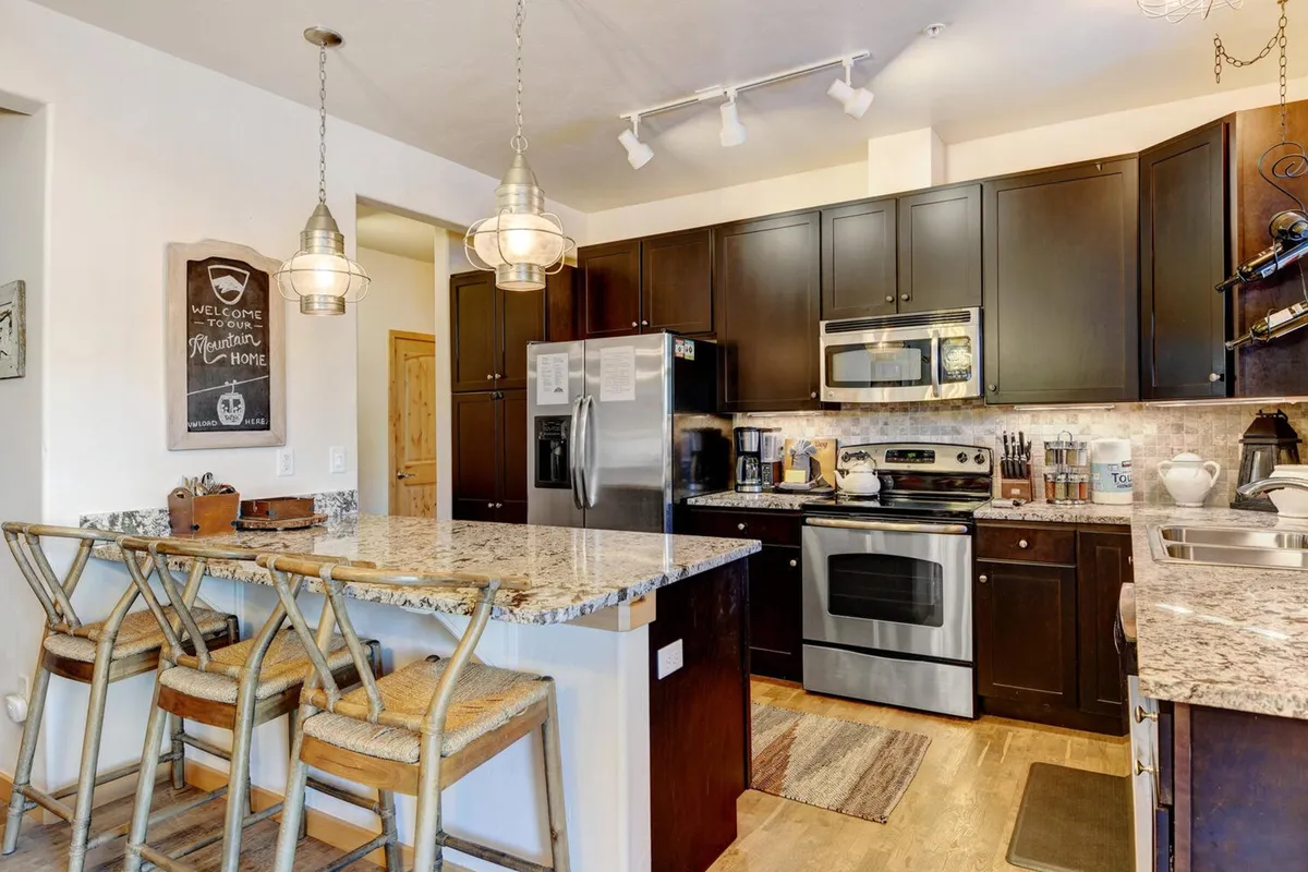 A modern chef’s kitchen showcasing gleaming granite countertops, stainless steel appliances, contemporary pendant lighting, and bar stools for casual dining. The space feels open, well-equipped, and ready for both cooking and entertaining.